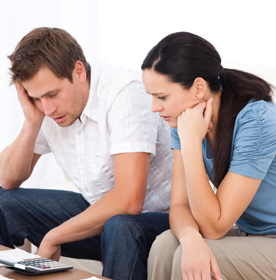 Couple looking concerned while reviewing insurance documents on a calculator, reflecting stress related to property damage claims.